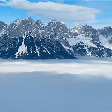 Eine beeindruckende Berglandschaft mit schneebedeckten Gipfeln. Darunter liegt ein Meer aus Nebel, das die Aussicht noch dramatischer macht.
