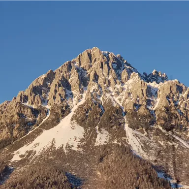 A majestic mountain with snow-capped peaks under a clear sky. The rocks are steep and impressive.