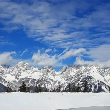 An impressive mountain landscape with snow-capped peaks under a clear blue sky. In the foreground, a snow-covered area is visible.