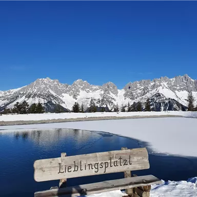 A beautiful viewpoint with a wooden sign "Favorite Place" and a view of snow-covered mountains. The calm lake reflects the clear blue sky.