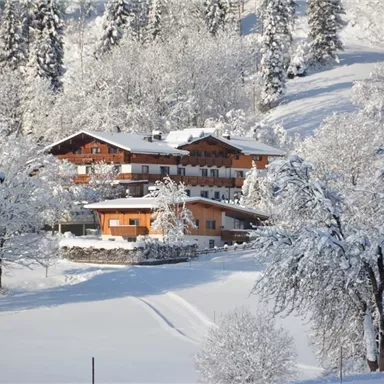 Eine verschneite Landschaft mit einem schönen Holzhaus. Die Bäume sind mit Schnee bedeckt und die Sonne scheint.