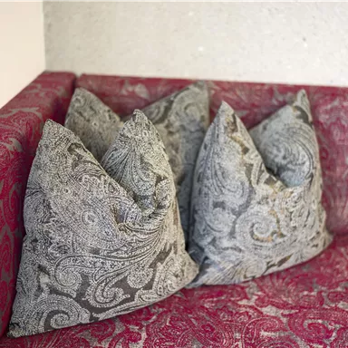 Ein Sofa mit drei dekorativen Kissen in grauem Muster. Die Sitzfläche hat einen roten Bezug mit floralem Design.
