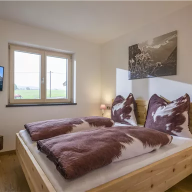 Ein gemütliches Schlafzimmer mit einem großen Bett und modernen Möbeln. An der Wand hängt ein Fernseher und es gibt ein Fenster mit Blick nach außen.