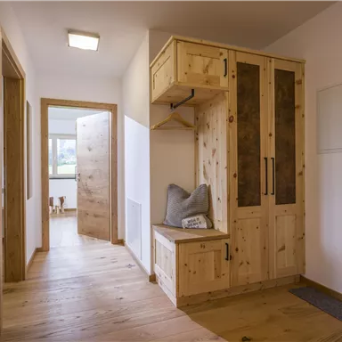 Ein heller Flur mit Holzfußboden und einem rustikalen Garderobenschrank. Der Raum wirkt einladend und modern.