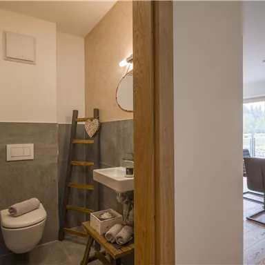 Ein modernes Badezimmer mit einer eleganten Toilette und einem Waschbecken. Im Hintergrund sieht man einen Essbereich mit Tisch und Stühlen.