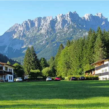 Eine malerische Landschaft mit zwei Gebäuden und einem großen, grünen Rasen. Im Hintergrund erhebt sich eine beeindruckende Bergkette.