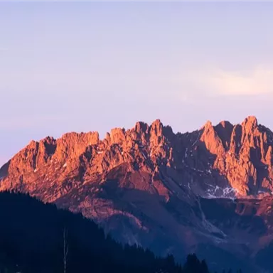 An impressive mountain landscape at sunset. The rocks radiate in warm, reddish tones.
