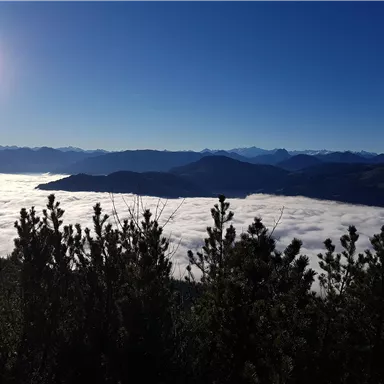 An impressive mountain landscape with clouds that look like an ocean below. The sky is clear and sunny.