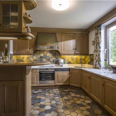 Eine moderne Küche mit Holzschränken und einem hellen, attraktiven Boden. Das Fenster bietet Blick ins Freie und sorgt für Tageslicht.