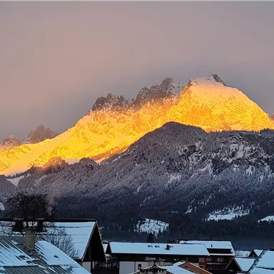 Ein beeindruckendes Bergpanorama mit einer schneebedeckten Landschaft. Die Gipfel leuchten golden im Licht der untergehenden Sonne.