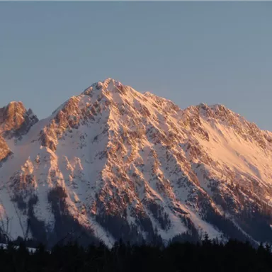 Ein schneebedeckter Berg mit steilen Felsen und goldenem Licht des Sonnenuntergangs. Die majestätische Landschaft strahlt Ruhe und Schönheit aus.