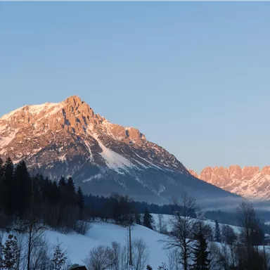 Eine beeindruckende Berglandschaft mit schneebedeckten Gipfeln und klarem Himmel. Die Sonne beleuchtet die Berge und schafft eine malerische Atmosphäre.