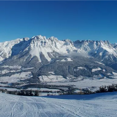Eine beeindruckende Berglandschaft mit schneebedeckten Gipfeln und klarem blauen Himmel. Die weite, verschneite Ebene verleiht der Szene eine friedliche Atmosphäre.