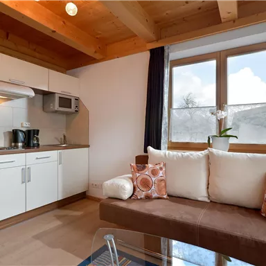 A modern living kitchen with a cozy couch and large windows. The combination of wood and white furniture creates an inviting atmosphere.