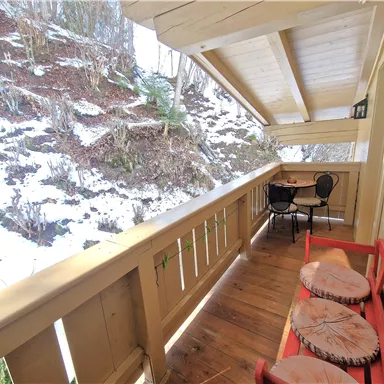 Ein gemütlicher Balkon mit einem roten Sitzbereich und einem kleinen Tisch. Im Hintergrund sind schneebedeckte Berge zu sehen.