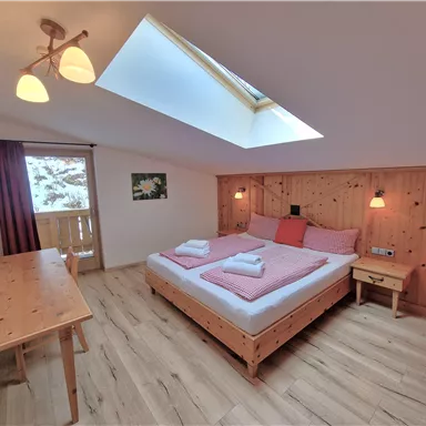Ein gemütliches Schlafzimmer mit einem Doppelbett und Holzdekor. Es gibt ein großes Fenster und einen Schreibtisch im Raum.