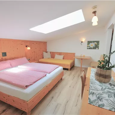 Ein gemütliches Schlafzimmer mit einem Doppelbett und einem Schlafsofa. Das Zimmer hat helle Wände, Holzverkleidung und viel natürliches Licht.