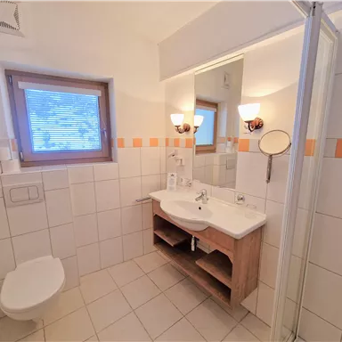 Ein modernes Badezimmer mit Dusche, Waschbecken und Spiegel. Die Wände sind hell gefliest, und es gibt ein Fenster, das Tageslicht hereinlässt.