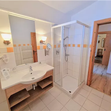 Ein modernes Badezimmer mit einer Duschkabine und einem Waschbecken. Die Wände sind hell gefliest und es gibt Holzdetails im Raum.