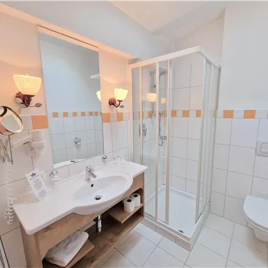 Ein modernes Badezimmer mit Dusche, Waschbecken und WC. Es ist hell und freundlich mit Fliesen in Weiß und Orange.