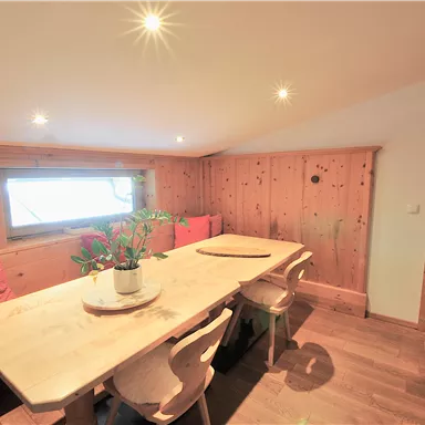 Ein gemütlicher Essbereich mit einem großen Holztisch und Stühlen. Die Wände sind aus Holz, und es gibt eine Fensterbank mit Pflanzen.