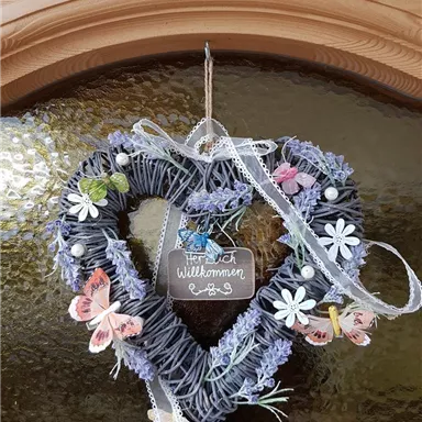 Ein dekorativer Herzkranz aus Naturmaterialien mit bunten Schmetterlingen und Blumen. Ein Schild mit der Aufschrift „Herzlich Willkommen“ verleiht ihm einen einladenden Charakter.