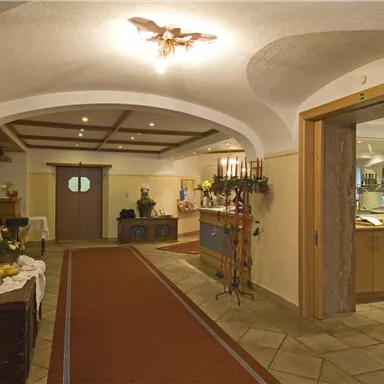 Ein einladender Eingangsbereich mit einem Teppich und warmem Licht. Auf der linken Seite stehen dekorative Möbel und Pflanzen.