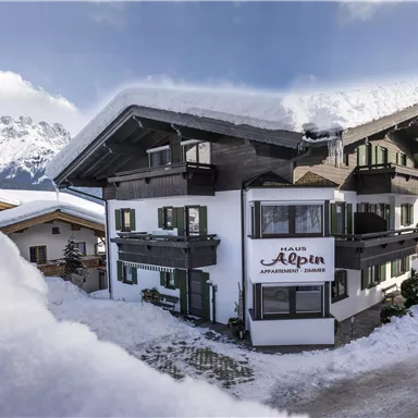 A cozy holiday home in the snow with mountains in the background. The surroundings are wintry and inviting.