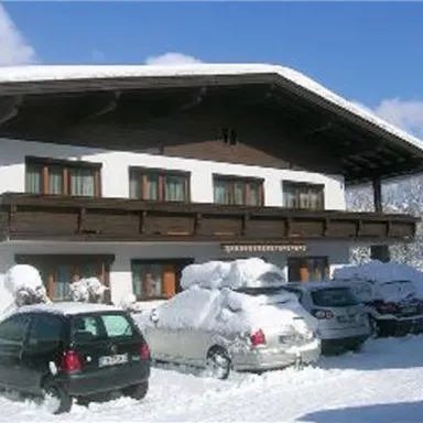 Ein Gebäude im Schnee mit einem großen Dach und Holzverkleidung. Autos sind unter einer dicken Schneedecke versteckt.