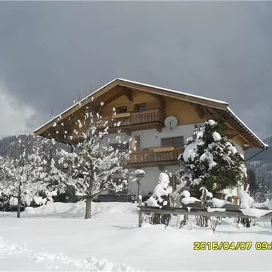 Ein charmantes Haus im Schnee mit schneebedeckten Bäumen. Der Himmel ist bewölkt, was eine winterliche Atmosphäre schafft.