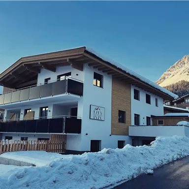 Ein modernes Gebäude im Schnee mit einem klaren blauen Himmel im Hintergrund. Die Umgebung zeigt wunderschöne Berge und eine ruhige Straße.