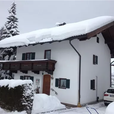 Ein weißes Haus im Schnee mit einem Balkon und grünen Fenstern. Der Garten ist festlich mit einer dicken Schneeschicht bedeckt.