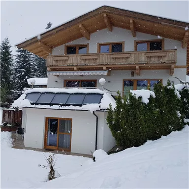 Ein modernes Haus mit Holzdetails, umgeben von Schnee. Flocken fallen sanft vom Himmel und die Umgebung ist friedlich und winterlich.