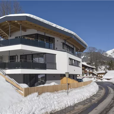 A modern house in the mountains, surrounded by snow. Snow-covered mountains are visible in the background.