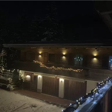 Ein gemütliches Chalet im Schnee, beleuchtet mit festlichen Lichtern. Der Nachthimmel sorgt für eine stimmungsvolle Atmosphäre.
