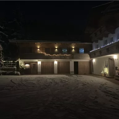Ein schönes, winterliches Haus bei Nacht, beleuchtet mit festlichen Lichtern. Der Schnee bedeckt den Boden und sorgt für eine gemütliche Atmosphäre.