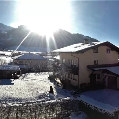 A snowy landscape with a large sunbeam in the background. In the foreground, some houses and mountains are visible.