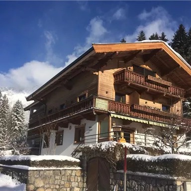 A charming chalet in winter with a snow-covered roof. Surrounded by fir trees and a clear blue sky.