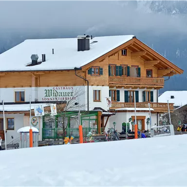 Ein traditionelles Holzhaus im Schnee, umgeben von Bergen. Die Atmosphäre ist gemütlich und einladend, ideal für einen Winterausflug.