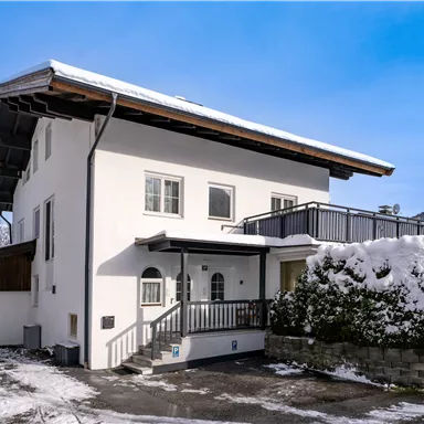 A modern house with a white facade and a balcony. The winter has covered the surroundings with snow.