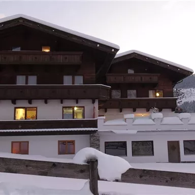 A cozy chalet in the snow with a warm light coming from the windows. Snow-covered mountains are visible in the background.