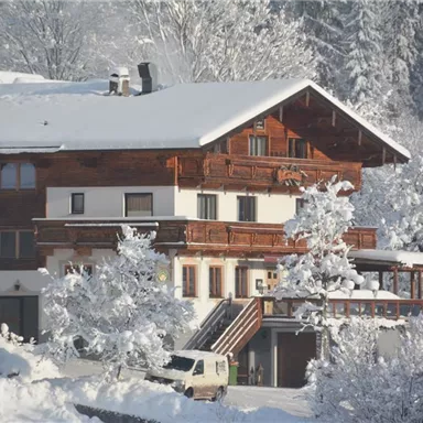Ein gemütliches Holzhaus im Schnee, umgeben von verschneiten Bäumen. Die Landschaft strahlt Ruhe und Winterzauber aus.