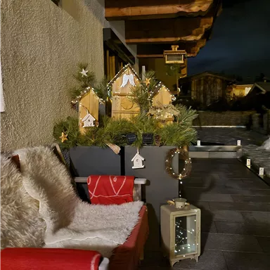 A cozy terrace with a wooden chair and soft blankets. Delicate Christmas decorations and a lantern create a festive atmosphere.