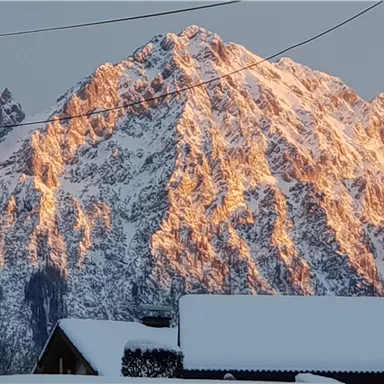 A majestic mountain with snow-covered peaks that shines warmly in the sunlight. In the foreground, snow-covered houses are visible.