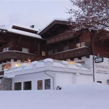 A cozy wooden house in the snow, surrounded by a winter landscape. The facade is traditionally designed with balconies and large windows.