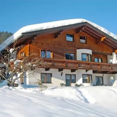 Ein charmantes Holzhaus im Schnee mit einem großen Dach. Die Umgebung ist winterlich mit frischem weißem Schnee.