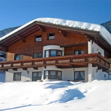 Ein charmantes Holzhaus mit einem schneebedeckten Dach. Die Umgebung ist von weißem Schnee und Bergen umgeben.