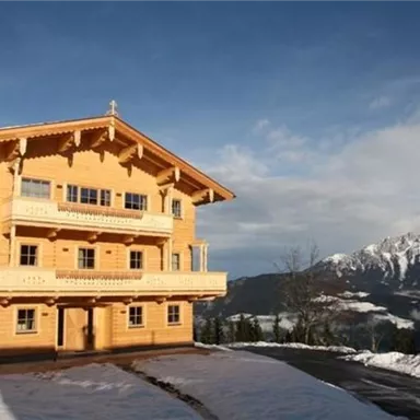 A beautiful wooden hut in the snow with an impressive mountain backdrop in the background. The sky is clear and the landscape is picturesque.