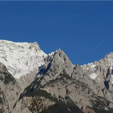 A majestic mountain landscape with snow-capped peaks and a clear blue sky. The rocks display impressive formations and are surrounded by beautiful nature.