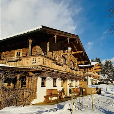 A traditional wooden house in the snow with a large balcony. The sky is clear and the surroundings exude a wintry calm.